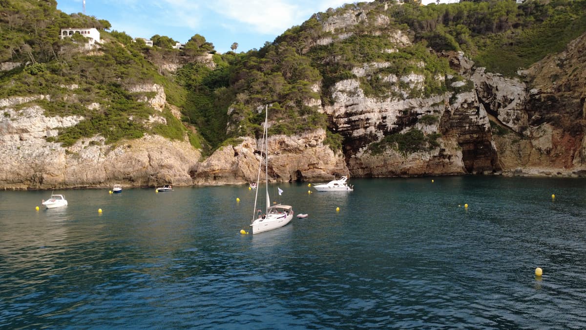 Velero y pequeñas embarcaciones fondeados en una cala rocosa de la Costa Blanca.